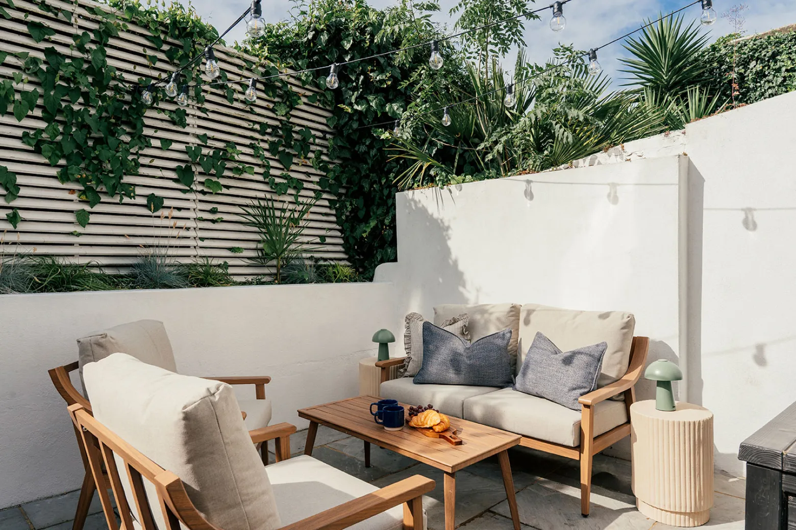 Sunlit courtyard garden with wooden sofa, armchairs and festoon lights