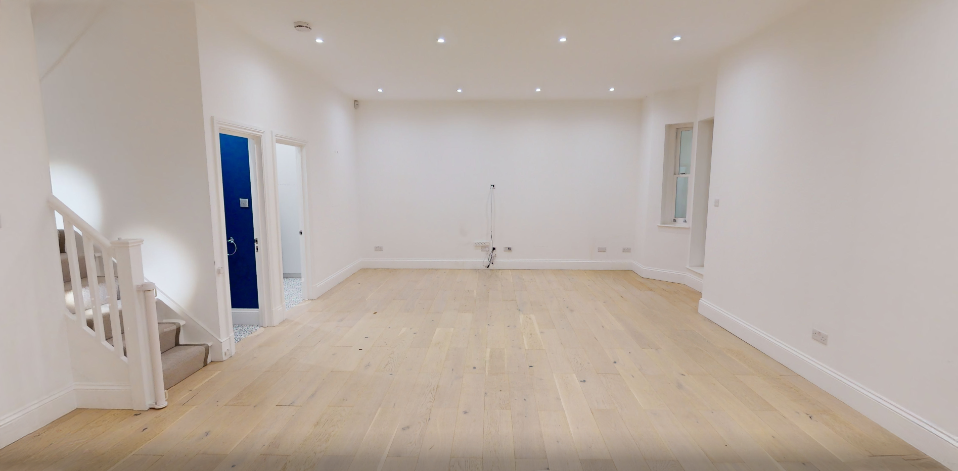 Empty unfurnished living room with pale walls, a single sash window and oak flooring