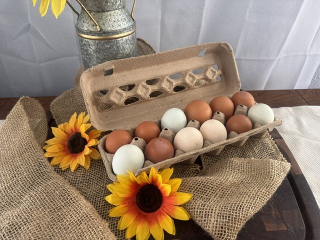 Carton of farm-fresh brown, cream and blue-green eggs on burlap with sunflowers