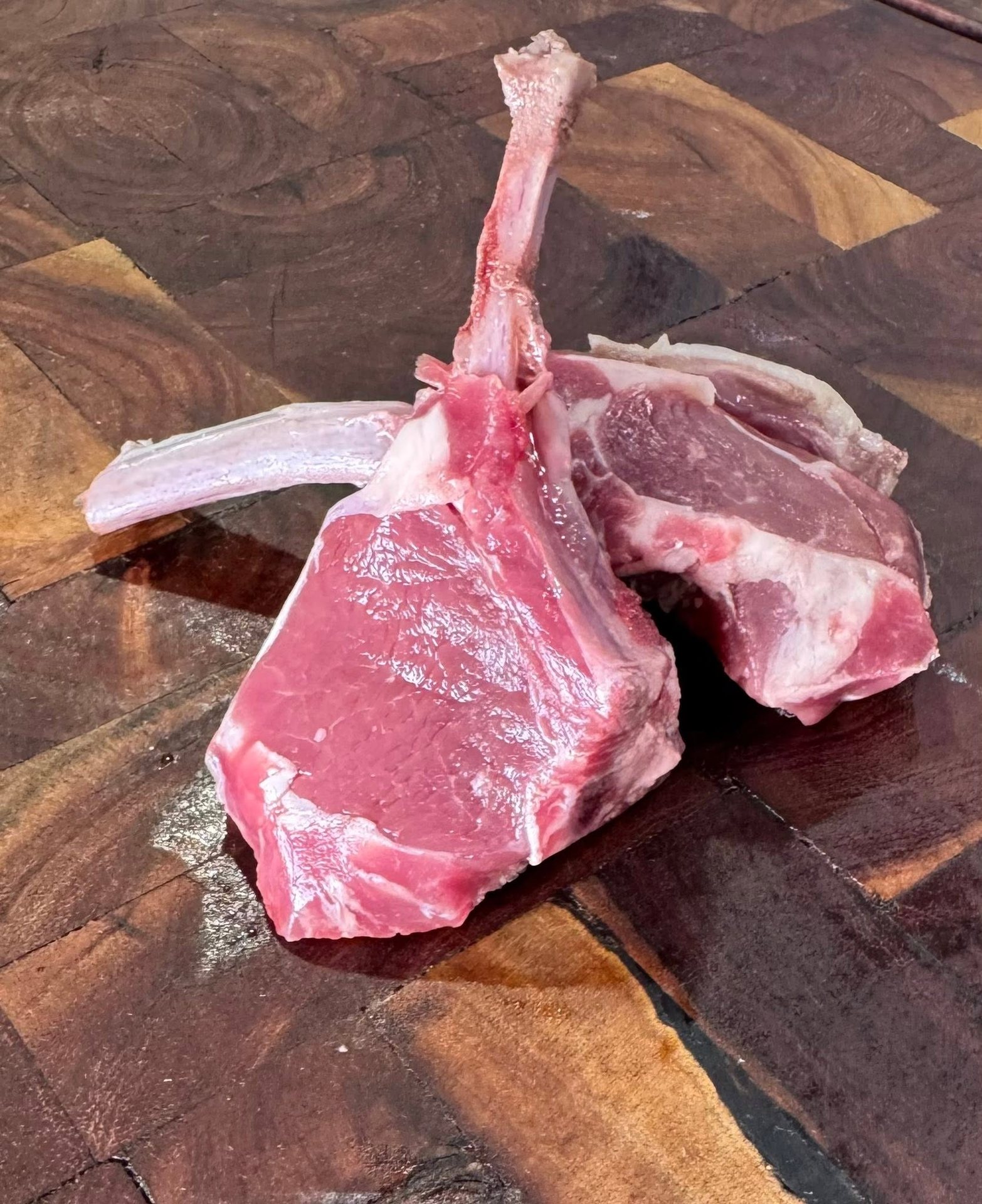 Two raw frenched bone-in pork chops on an end-grain wooden cutting board