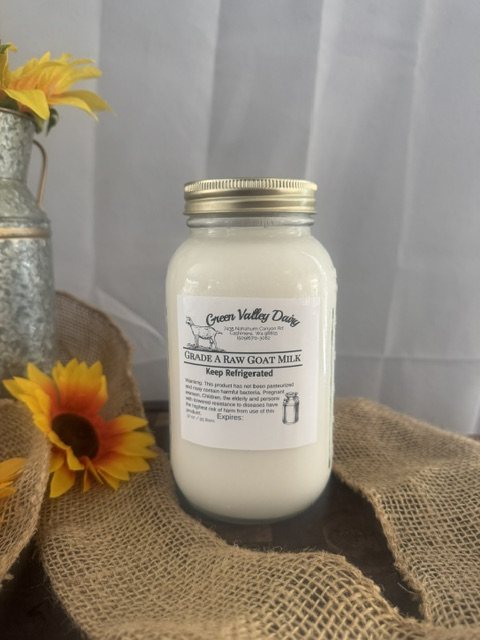 Quart jar of Green Valley Dairy Grade A raw goat milk on burlap beside a sunflower