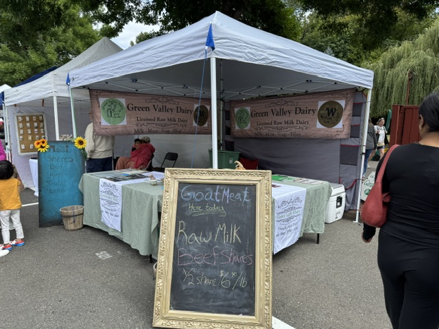 Green Valley Dairy farmers market tent with a chalkboard advertising goat meat, raw milk and beef shares