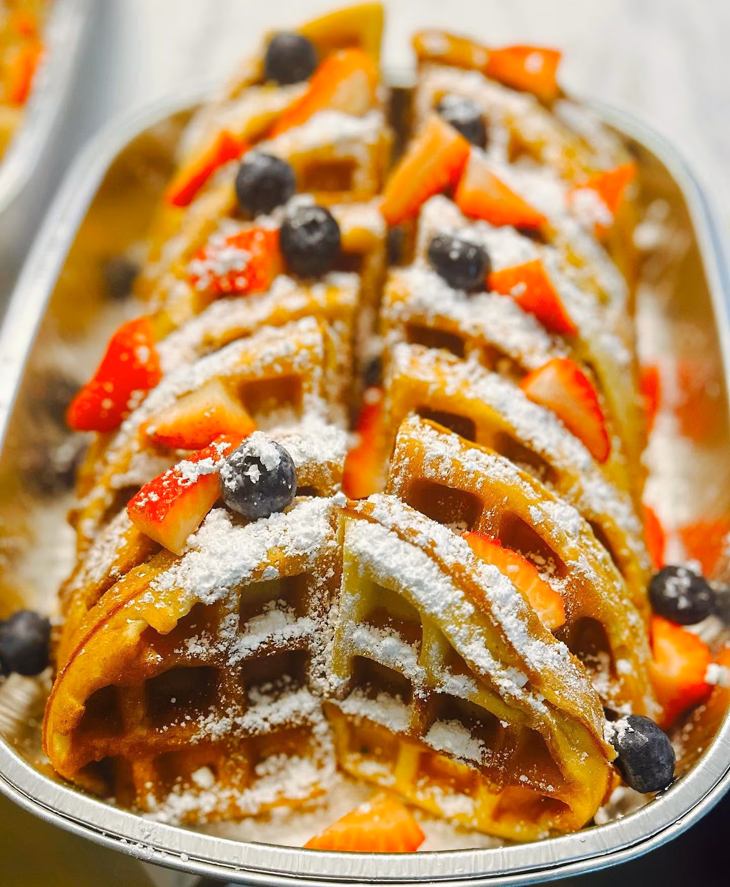 A waffle with strawberries and blueberries on top.