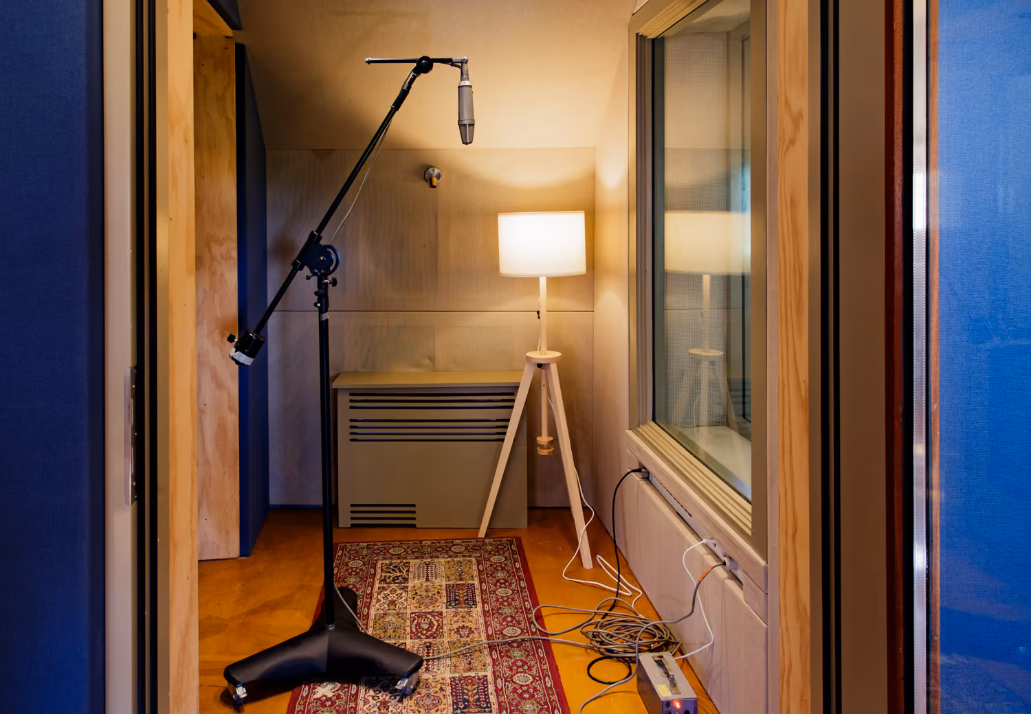 Booth 1 in Studio 1 with a condenser mic on a boom stand, tripod floor lamp, Persian runner and coiled cables
