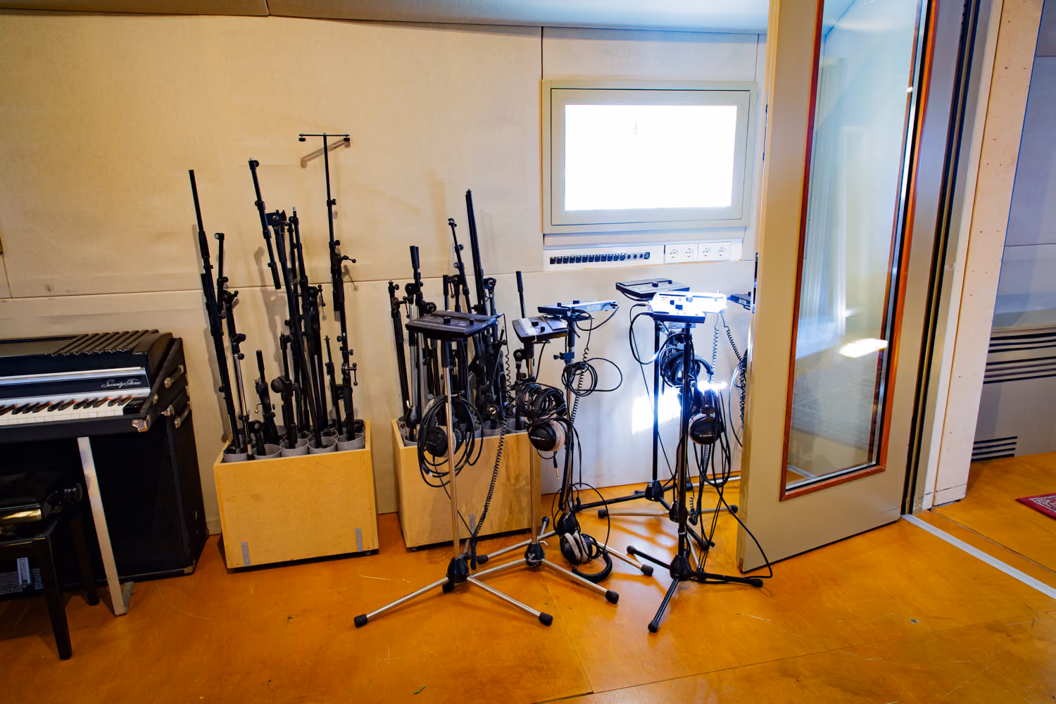Studio 1 live room corner with mic stands in wooden bins, headphone mixers with headphones and a Rhodes electric piano