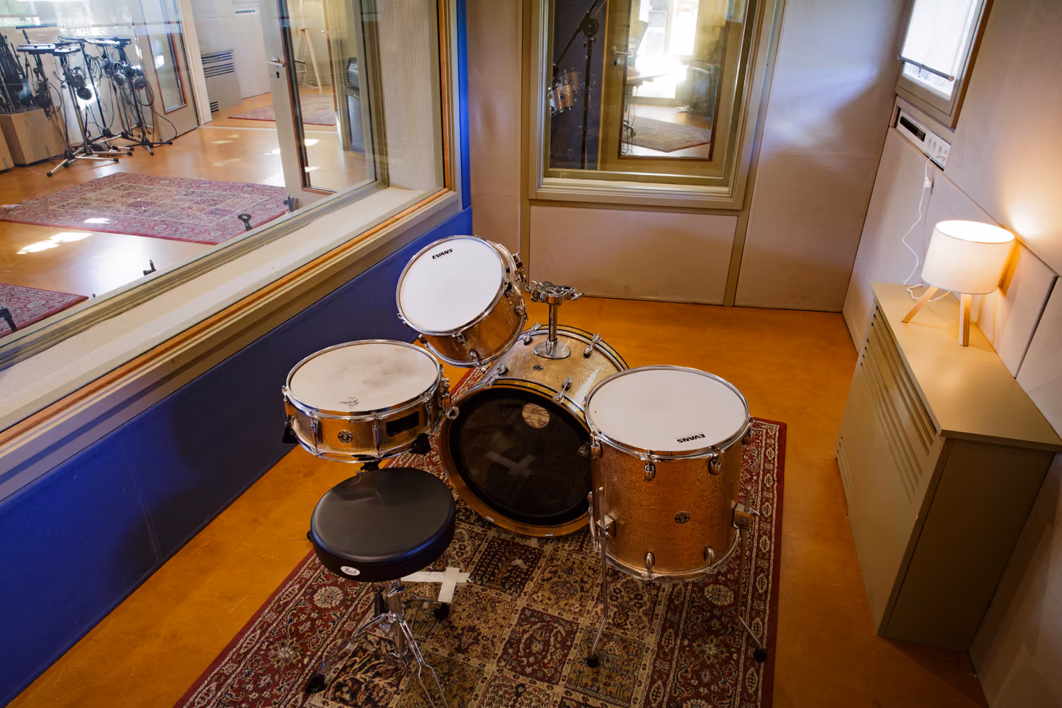 Isolation booth with a gold sparkle drum kit on a Persian rug, large window looking into the Studio 1 live room
