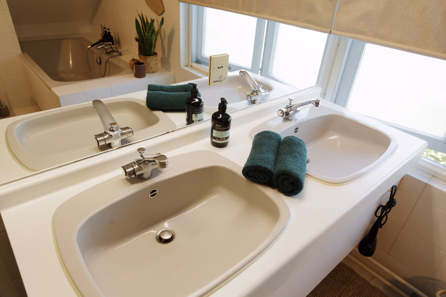 Shared bathroom upstairs with two sinks, rolled teal towels and soap bottles, a bathtub reflected in the mirror