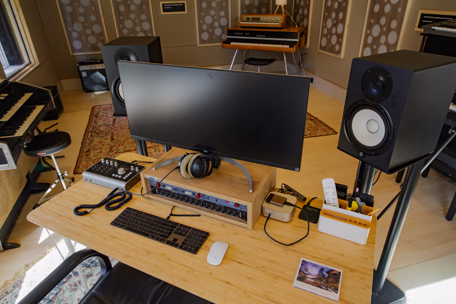 Studio 2 desk with an ultrawide monitor, Yamaha speakers, headphones and audio interface, vintage keyboards behind