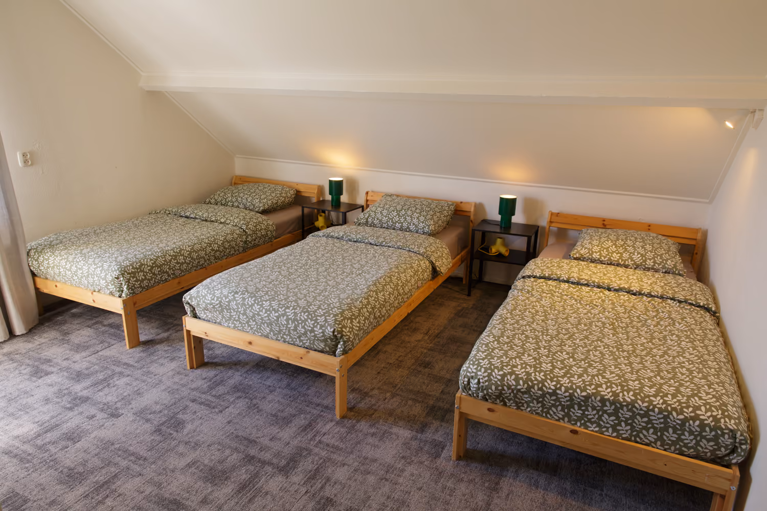 Bedroom upstairs with three single pine beds, green leaf-print bedding and green bedside lamps under a sloping ceiling