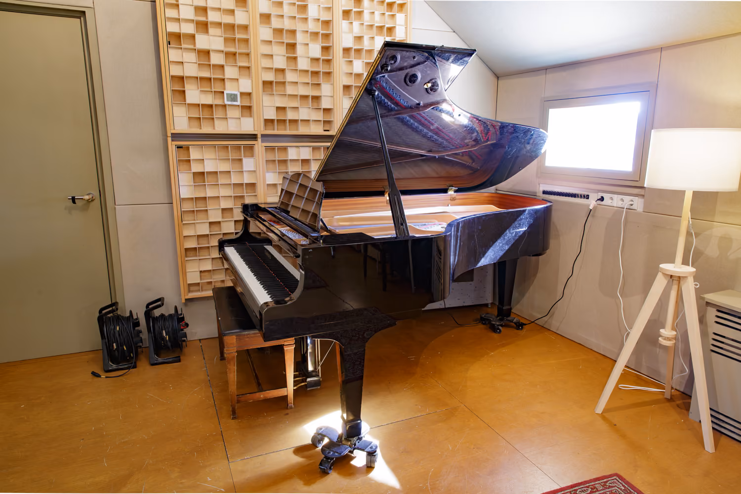 Studio 1 live room with a black grand piano beside wooden diffuser panels, cable reels and a tripod floor lamp