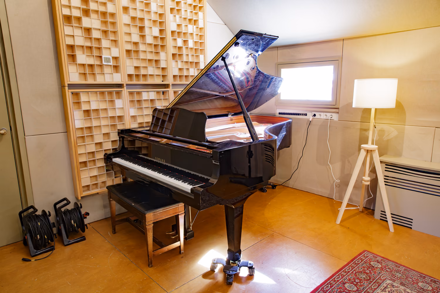 Yamaha grand piano with its lid raised in front of wooden diffuser panels in the Studio 1 live room