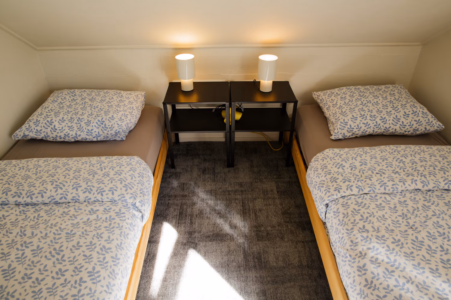 Bedroom upstairs with two single beds in blue leaf-print bedding and white lamps on black nightstands