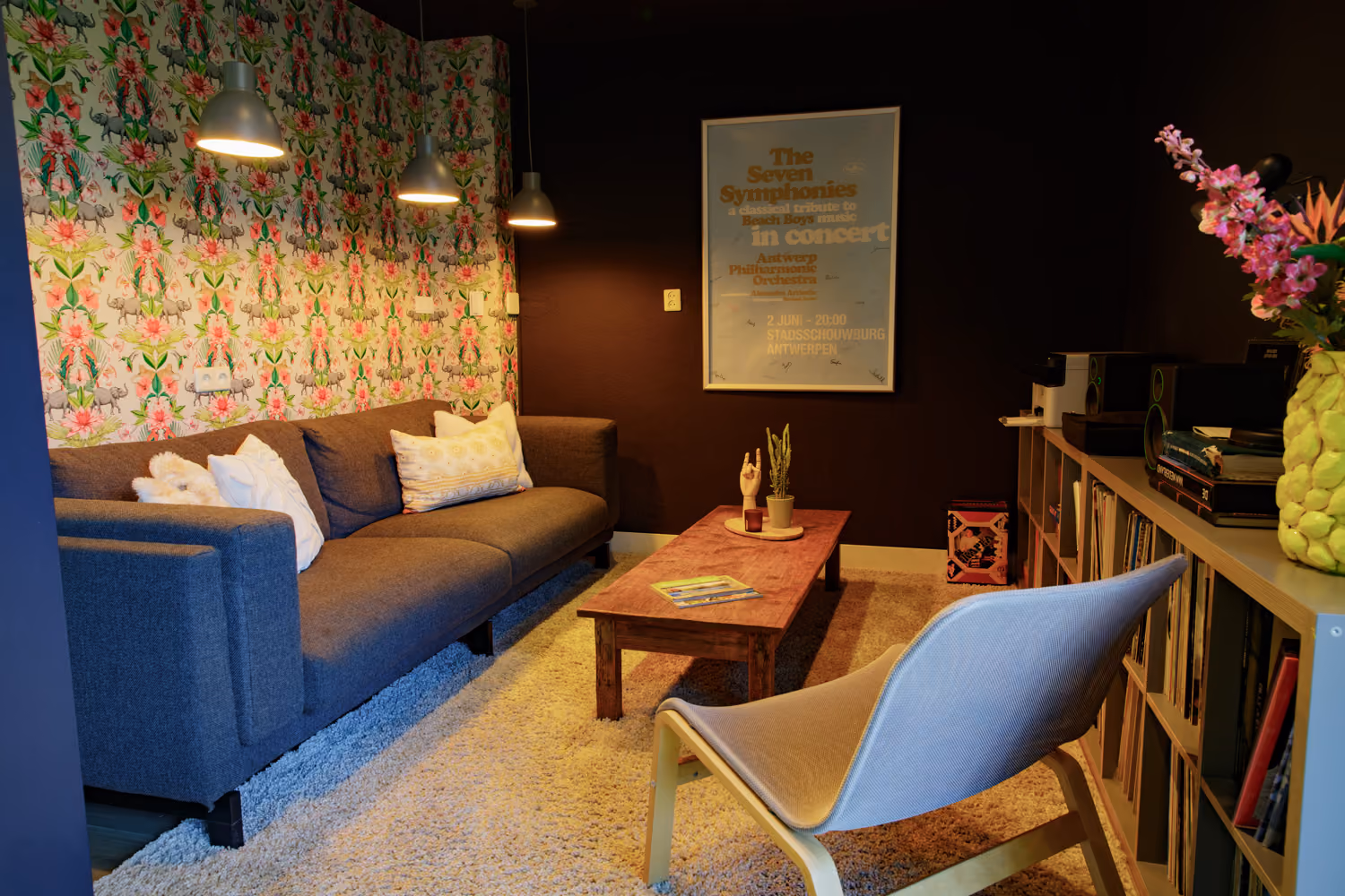 Guest area living room with dark walls, a grey sofa, floral elephant wallpaper and shelves of vinyl records