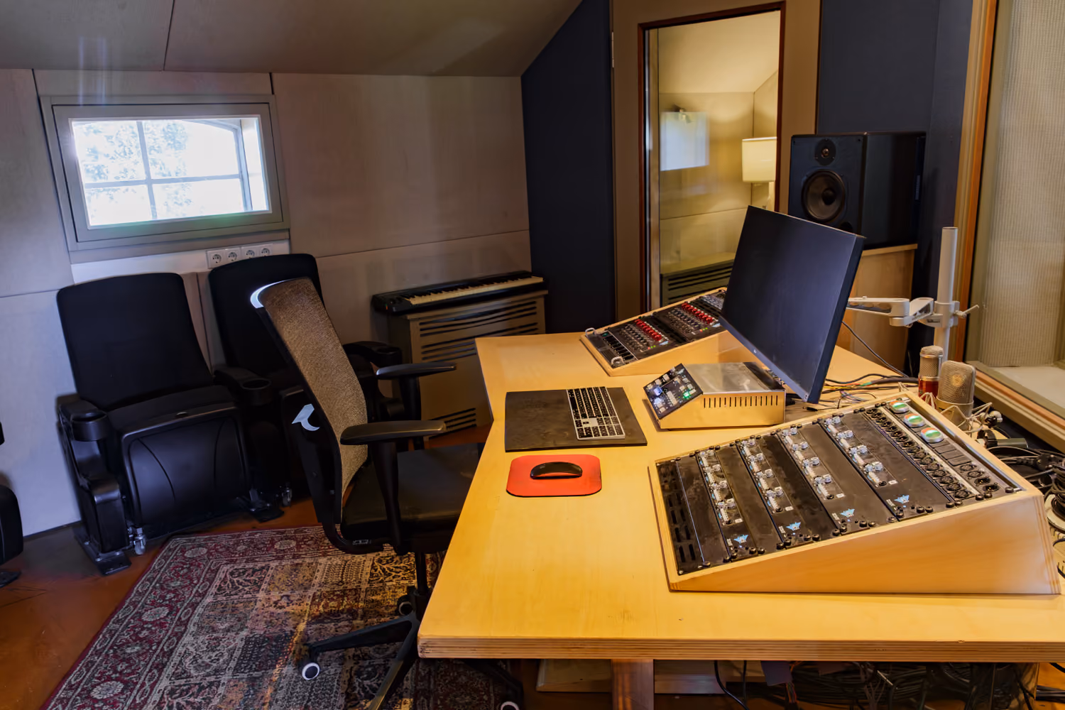 Studio 1 control room desk with an angled API preamp rack, monitor, keyboard and cinema seats by a small window