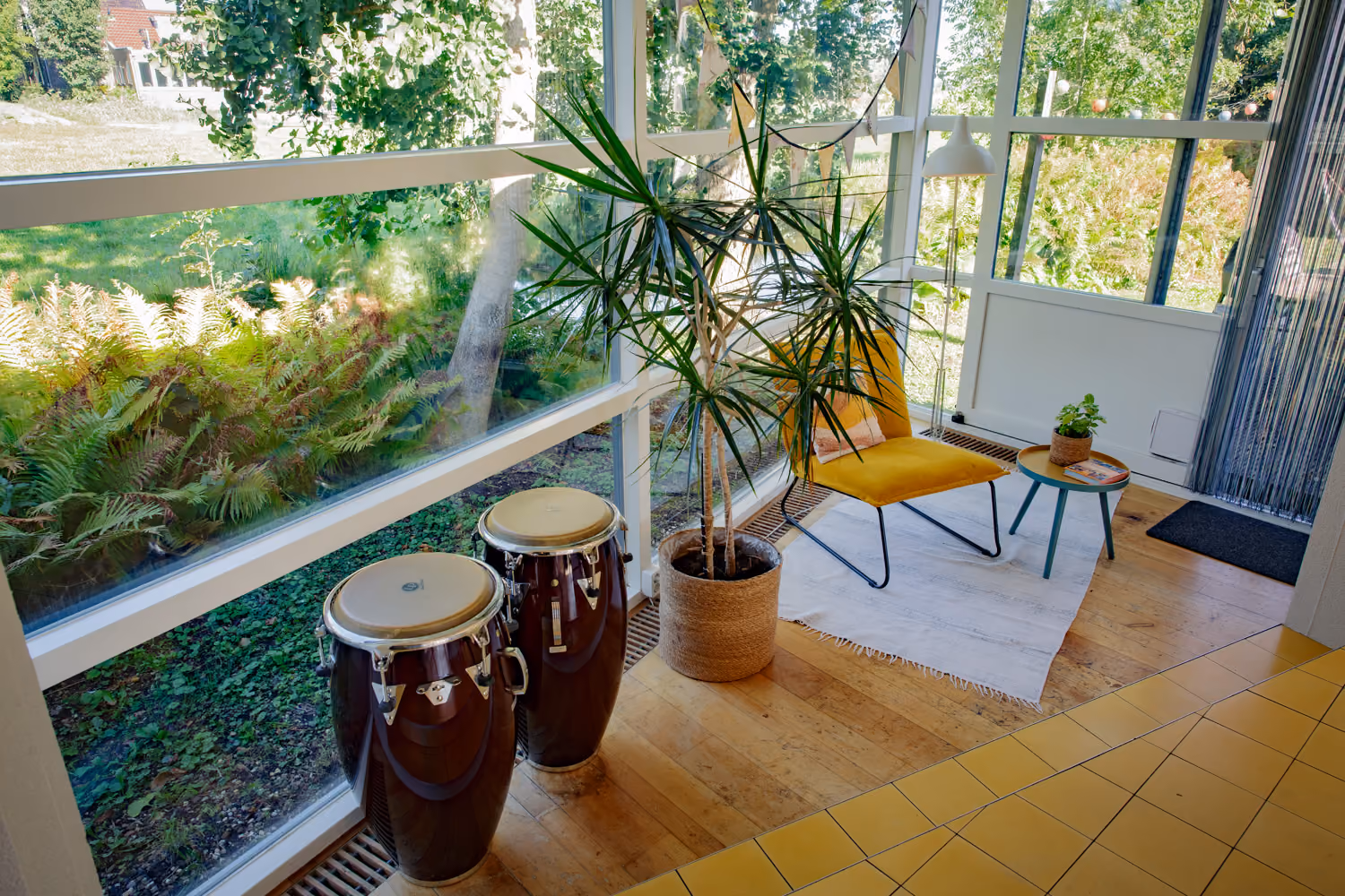 Guest area chill corner by big windows with two conga drums, a potted palm and a yellow lounge chair