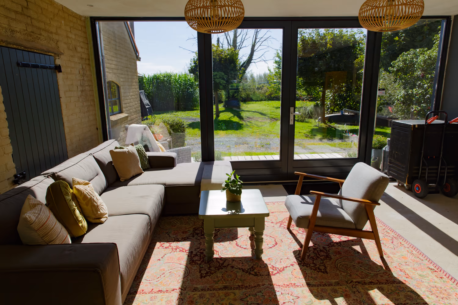 Guest area chill corner with a grey corner sofa, Persian rug and floor-to-ceiling glass doors onto the garden