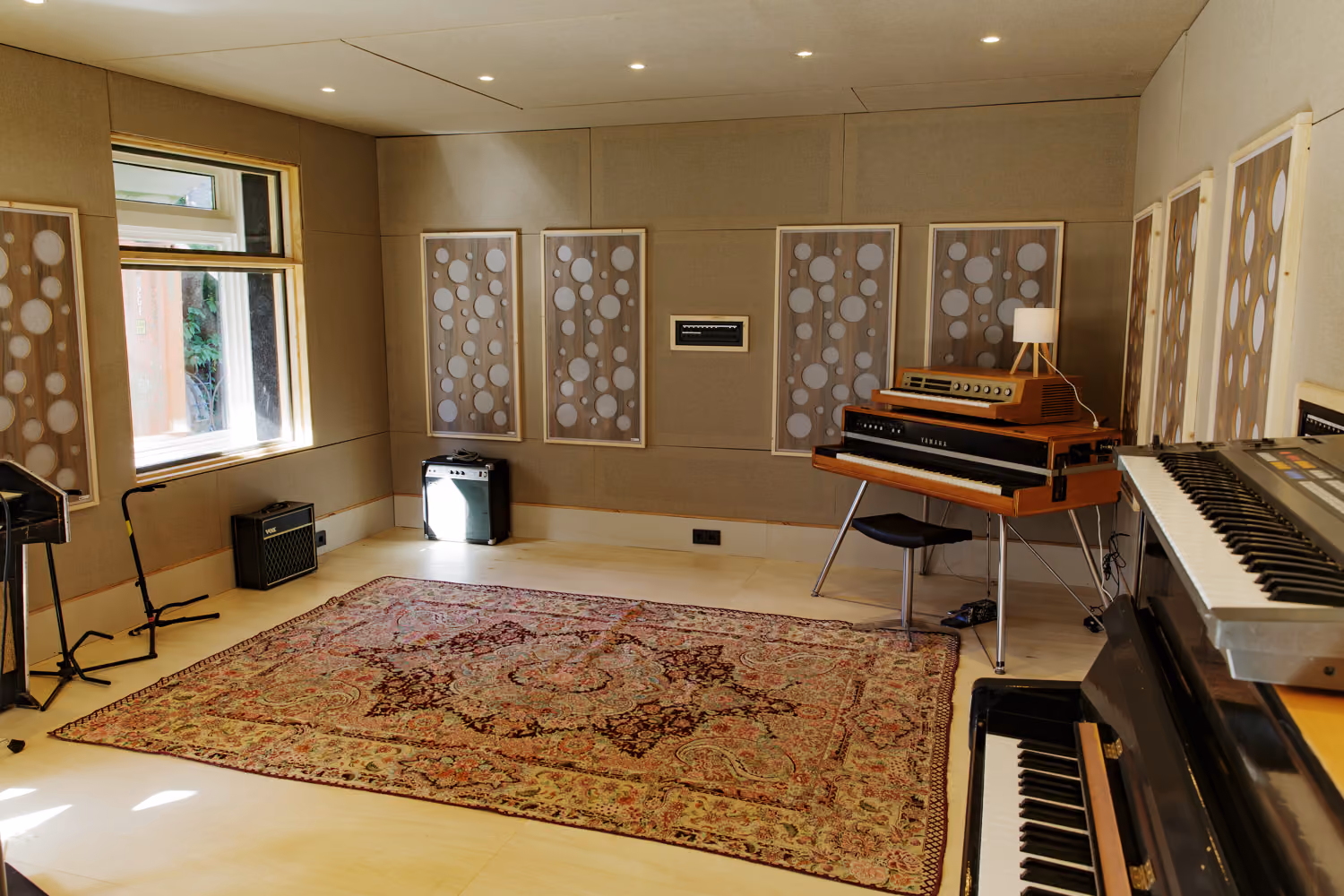 Studio 2 daylight room with vintage Yamaha keys, an upright piano, combo amps and a Persian rug on a light wood floor