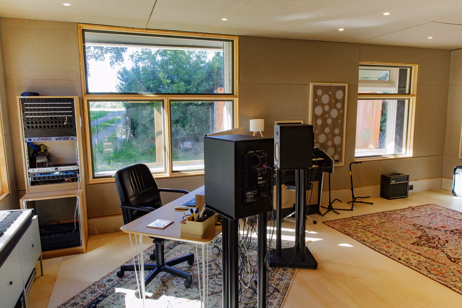 Studio 2 production room with large windows onto the garden, Yamaha monitors on stands, a desk and Persian rugs