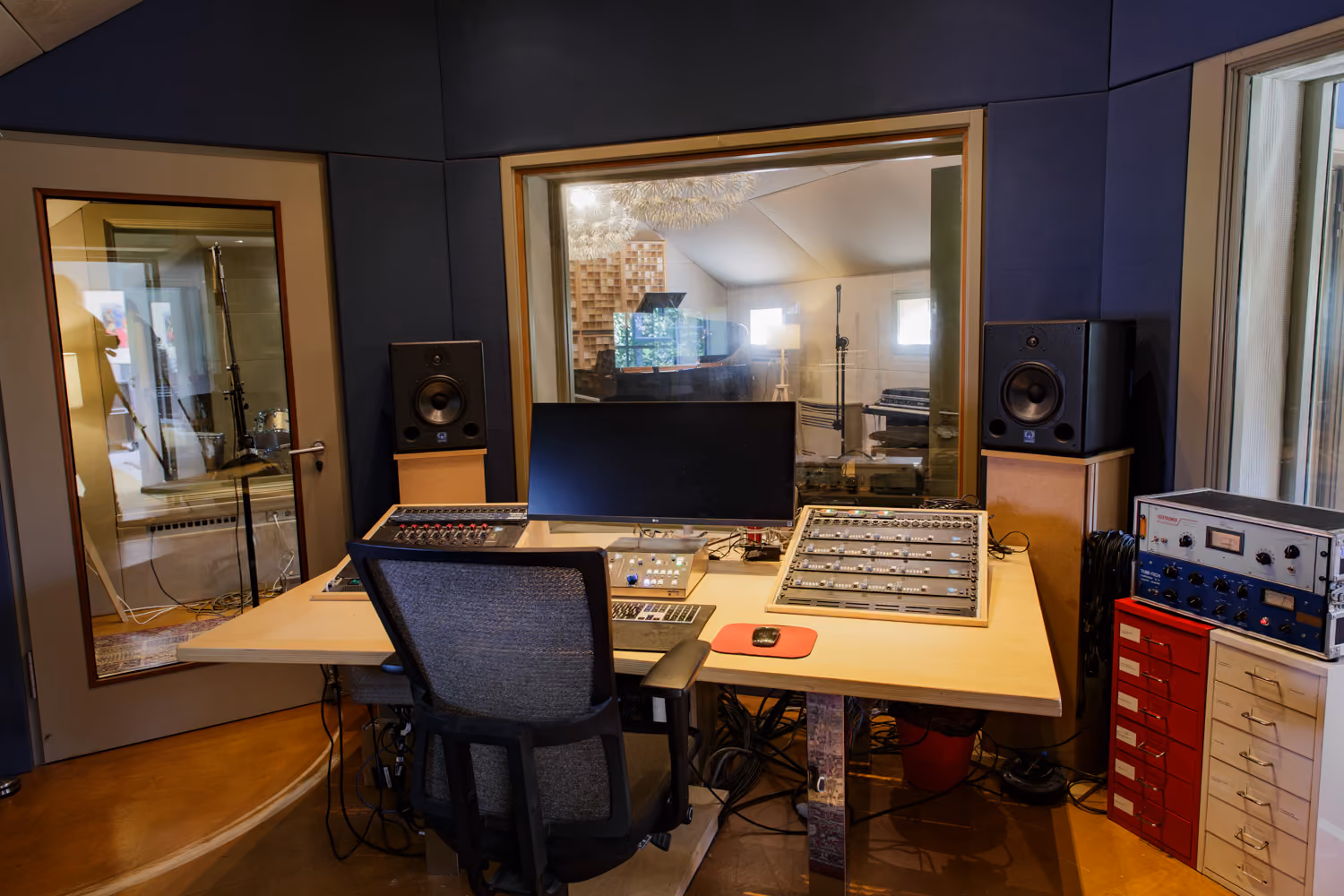 Studio 1 control room desk with studio monitors, outboard gear and a window looking into the live room
