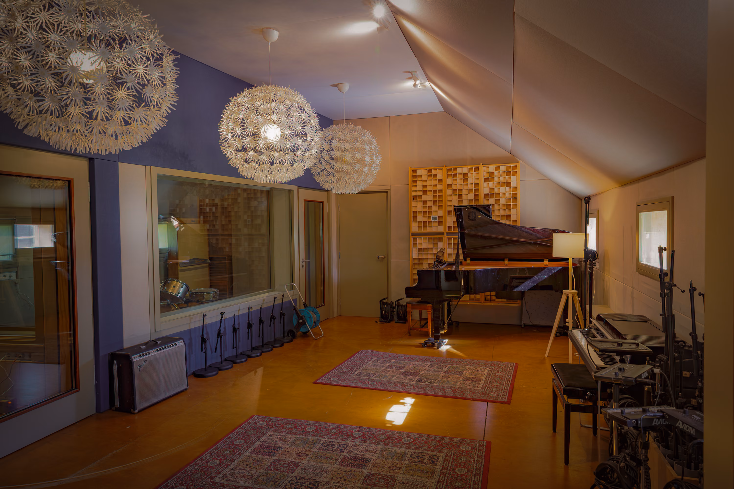 Studio 1 live room with a grand piano, pendant lamps, Persian rugs and a window into a drum booth
