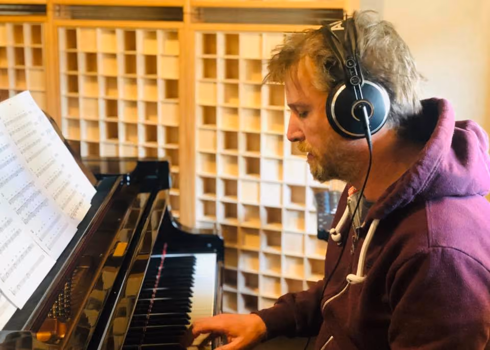 Musician wearing headphones playing the grand piano in the Studio 1 live room, with wooden diffusers behind