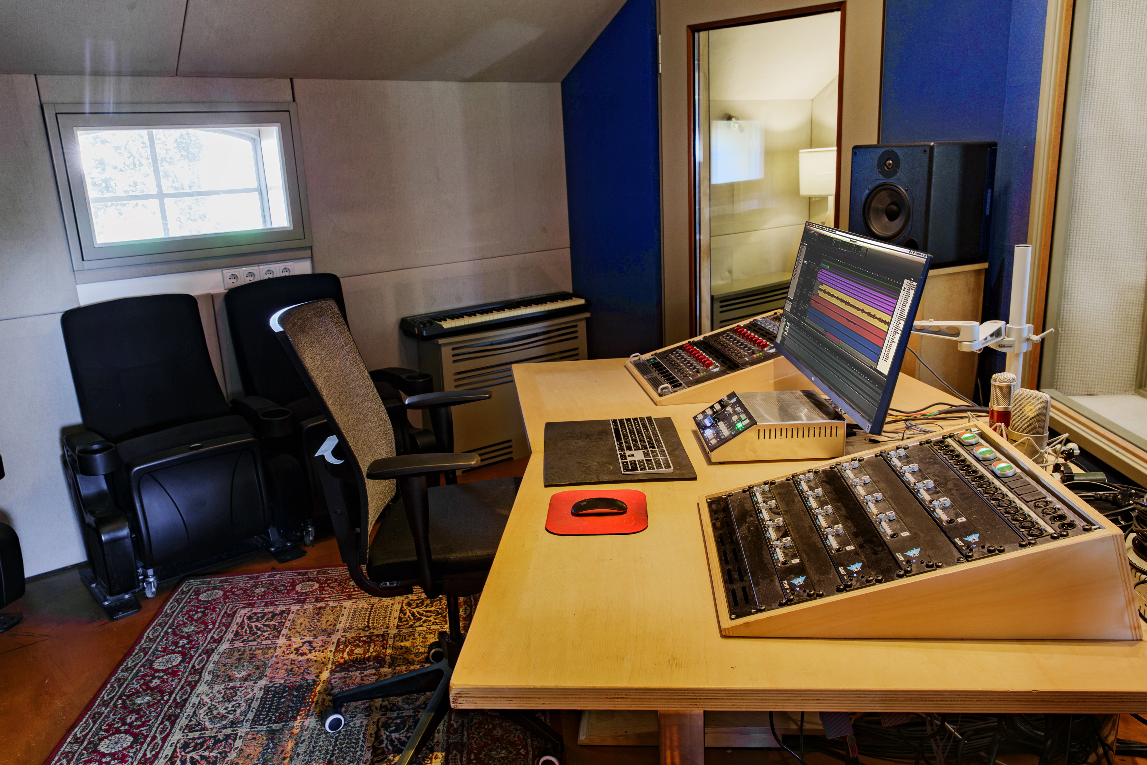 Studio 1 control room desk with an angled API preamp rack, a monitor, a keyboard and two cinema seats by a small window