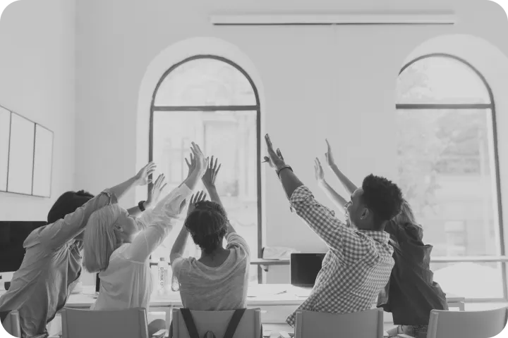 A team raising their hands together in a meeting room