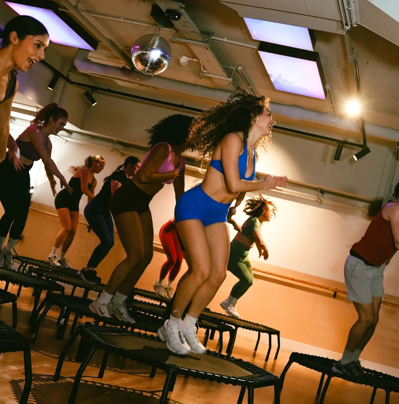 A group of people participating in a trampoline fitness class indoors, jumping on individual mini trampolines with energetic expressions.