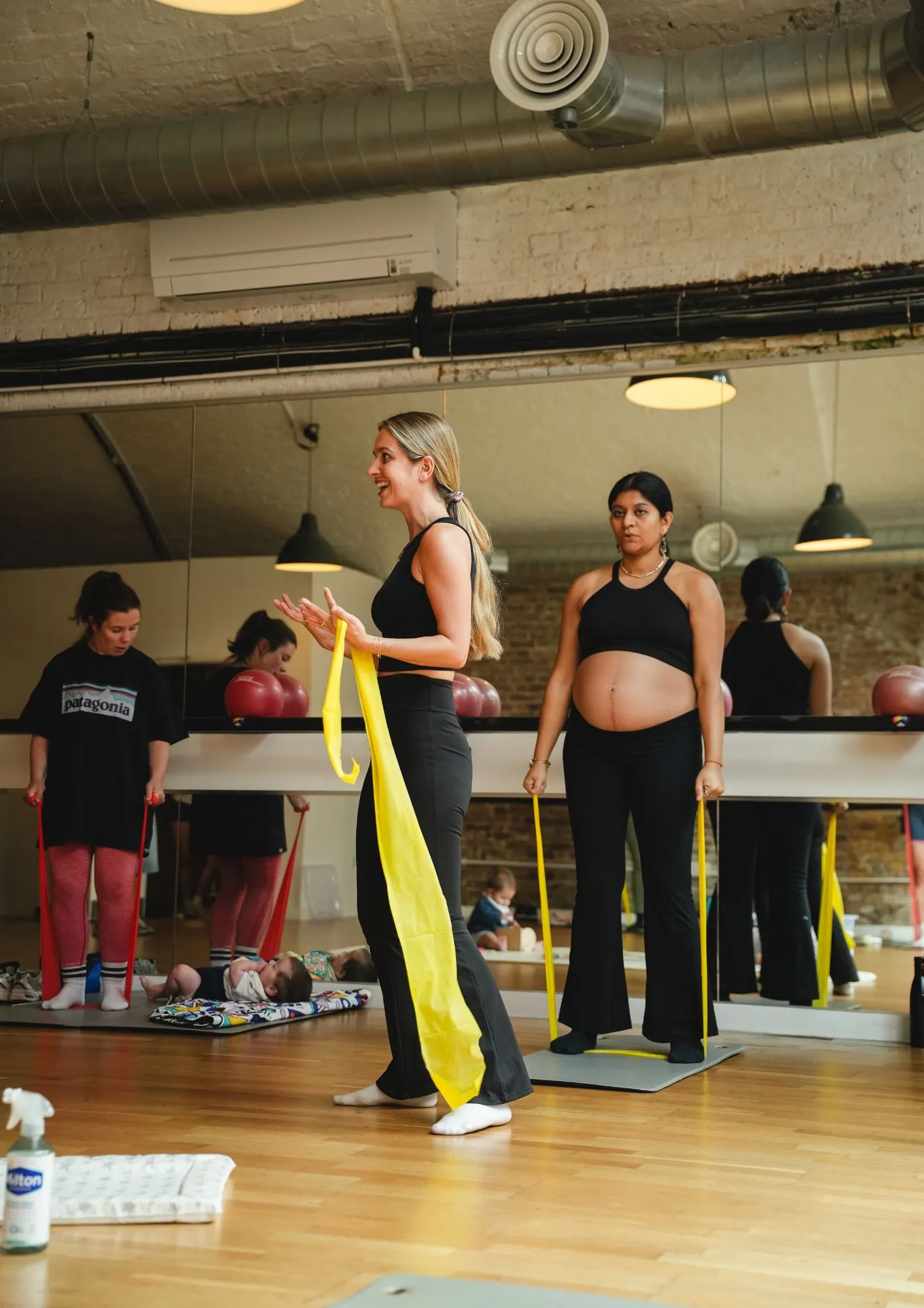 Instructor demonstrating a resistance band exercise to a pregnant woman and class at the barre