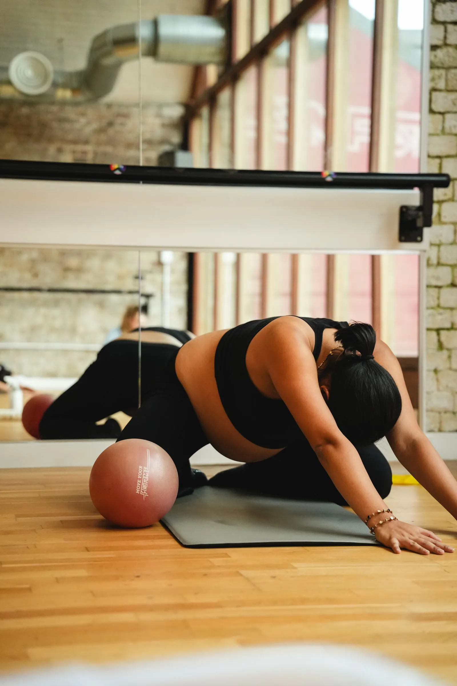 Pregnant woman resting in a child's pose stretch on a mat next to a Pilates ball