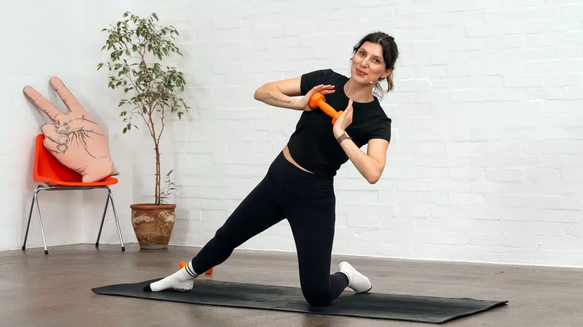 Woman doing a kneeling side stretch with a small weight on a mat in a white studio