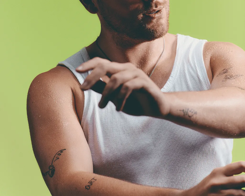 Man with tattooed arms in a white vest against a green background