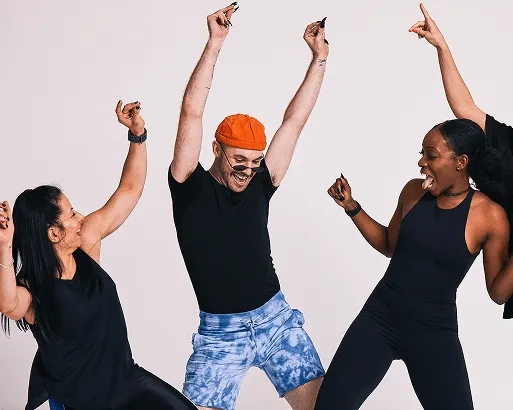 Three people dancing with arms raised in black outfits against a white backdrop