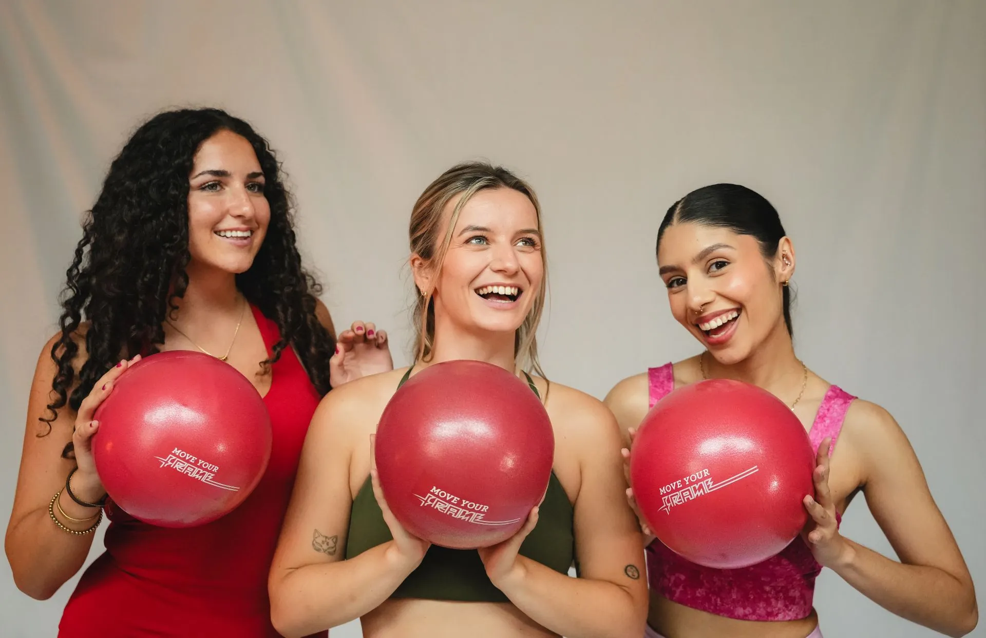 Three smiling women each holding a red Pilates ball