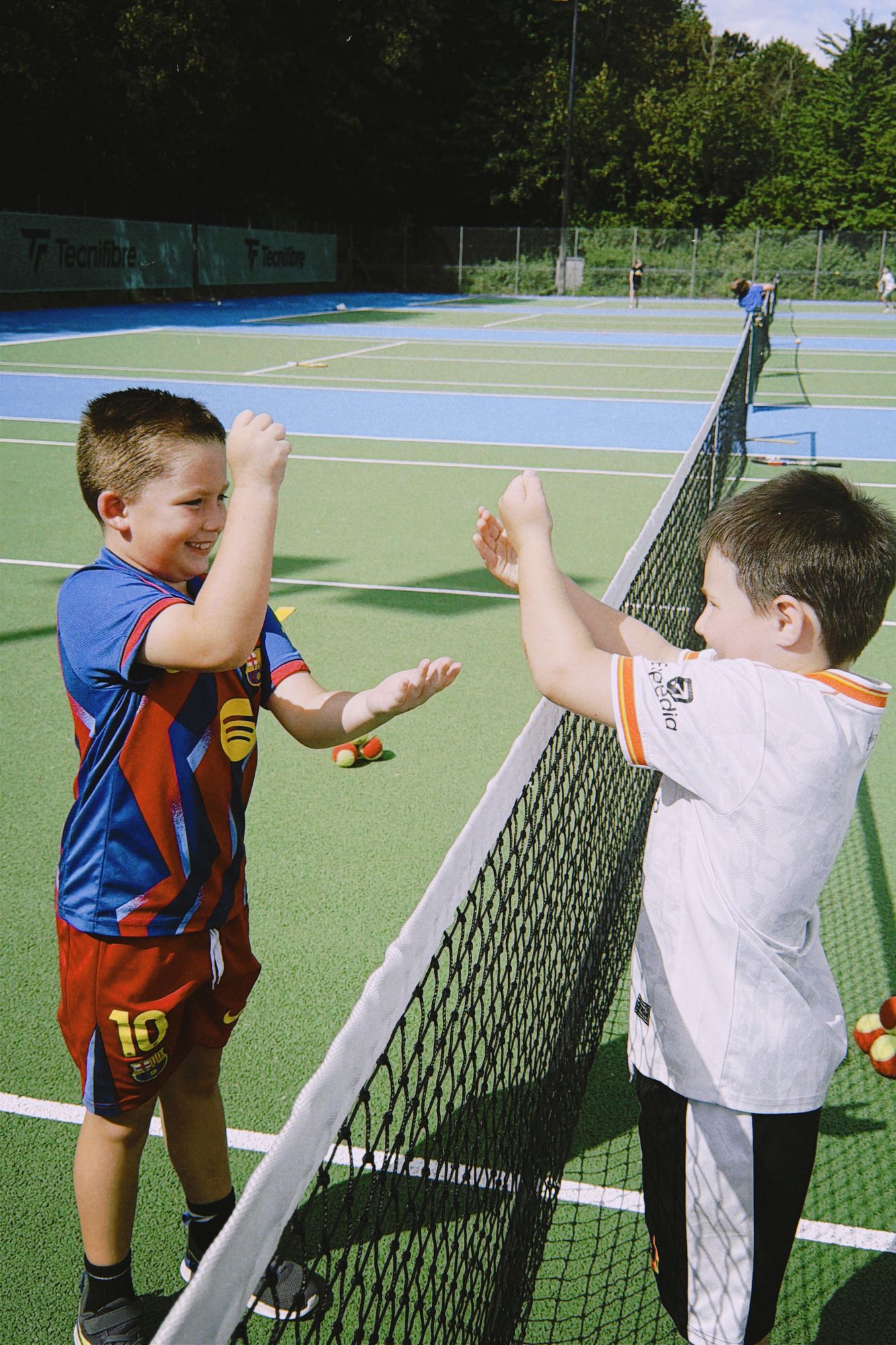 Two young players high-fiving over the net on the outdoor courts