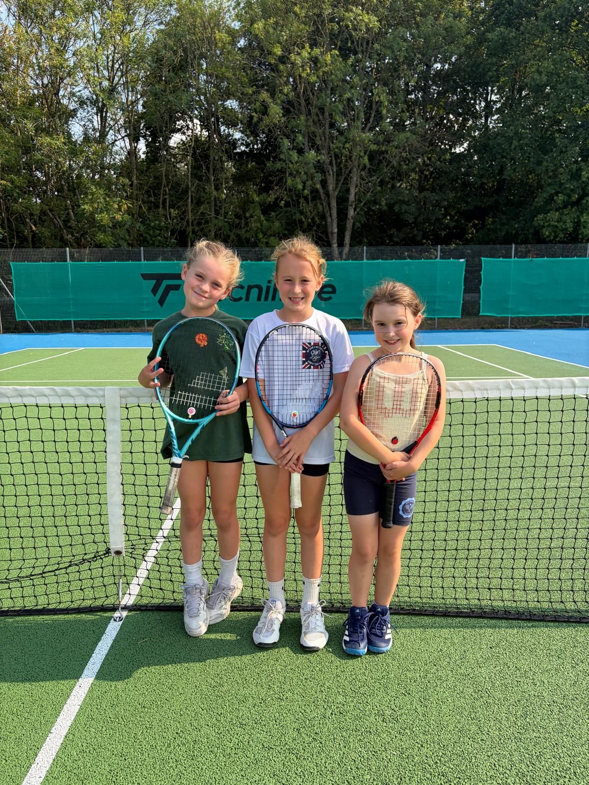 Three young players with their rackets at the net on the outdoor courts