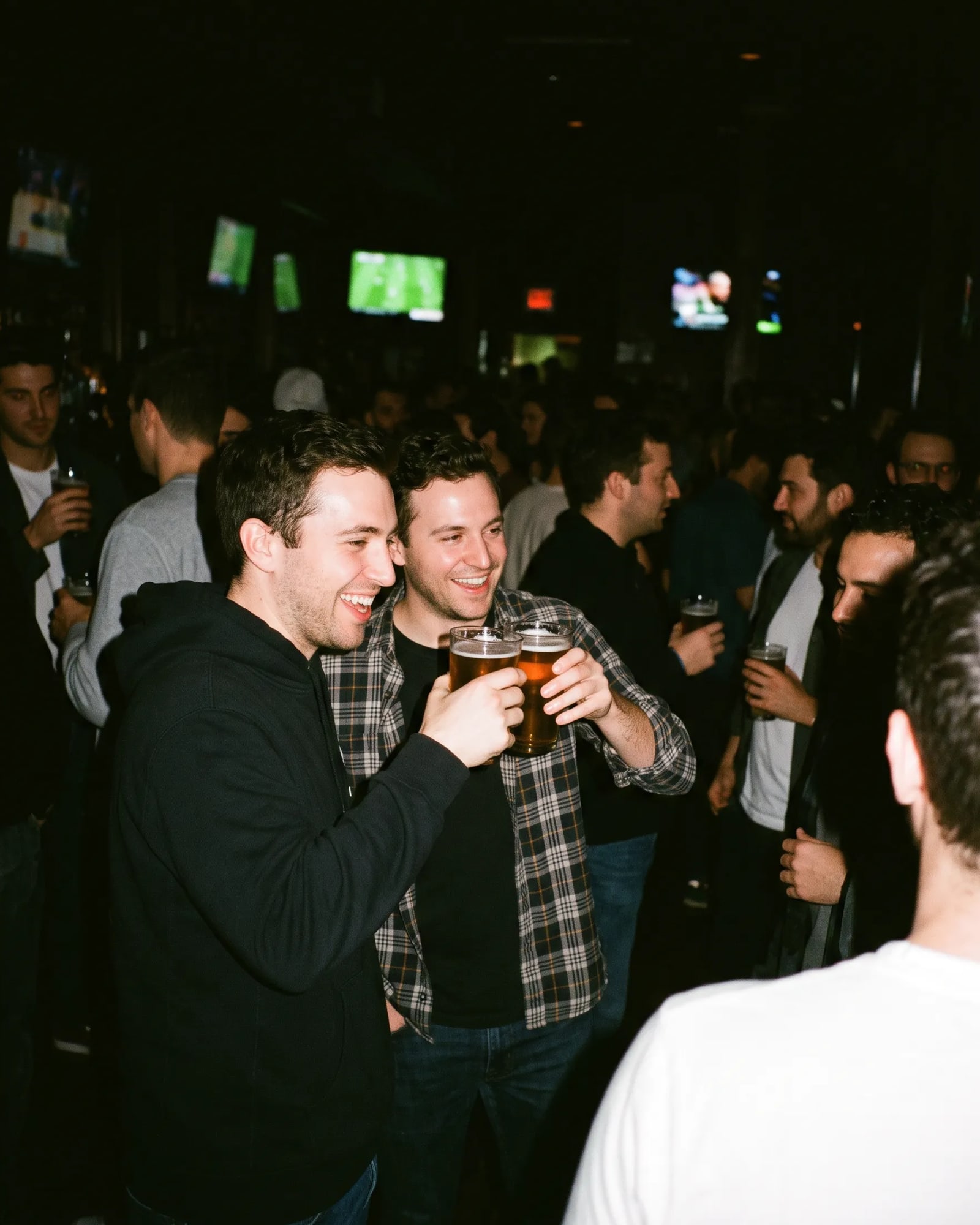Two friends raising glasses at a crowded sports bar.
