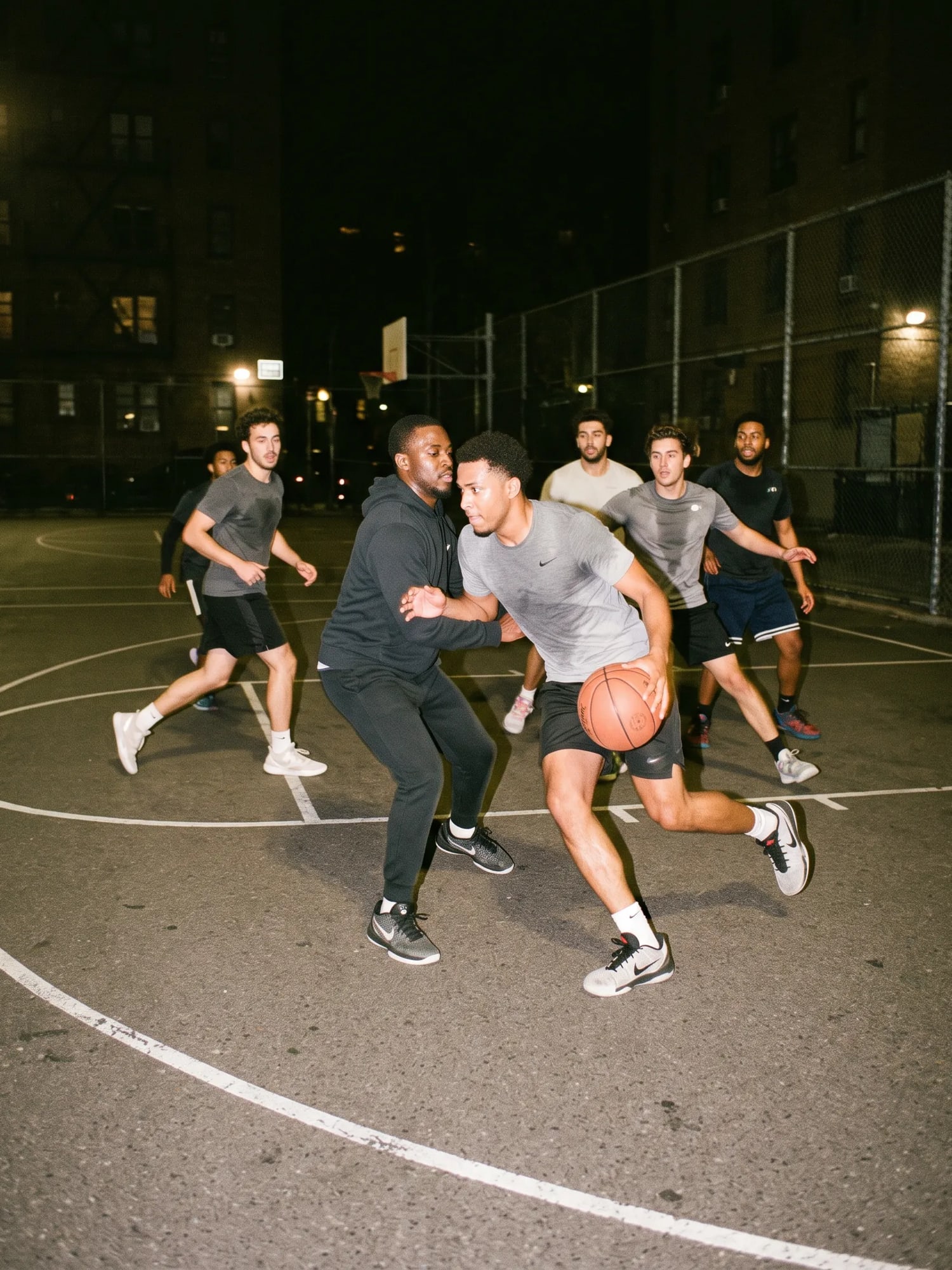 A pickup basketball game on an outdoor court under night lights.