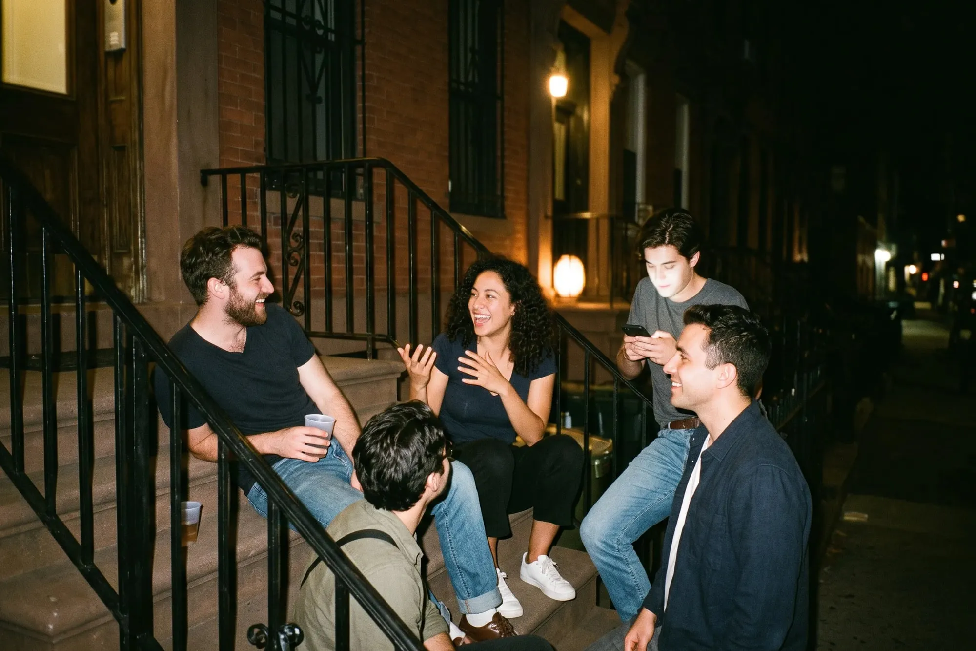 Friends laughing on a brownstone stoop at night.