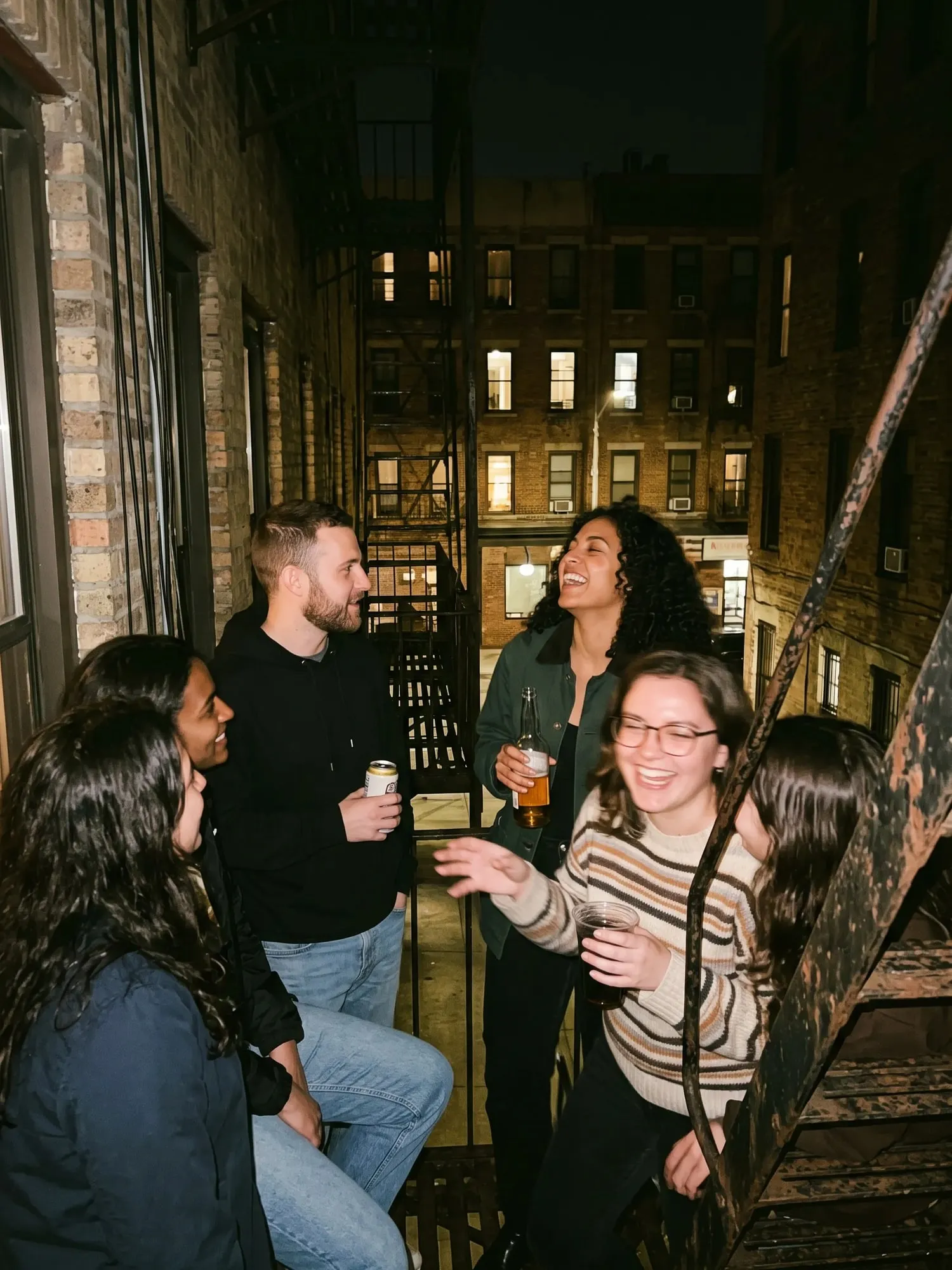 Friends with drinks on a fire escape at night.