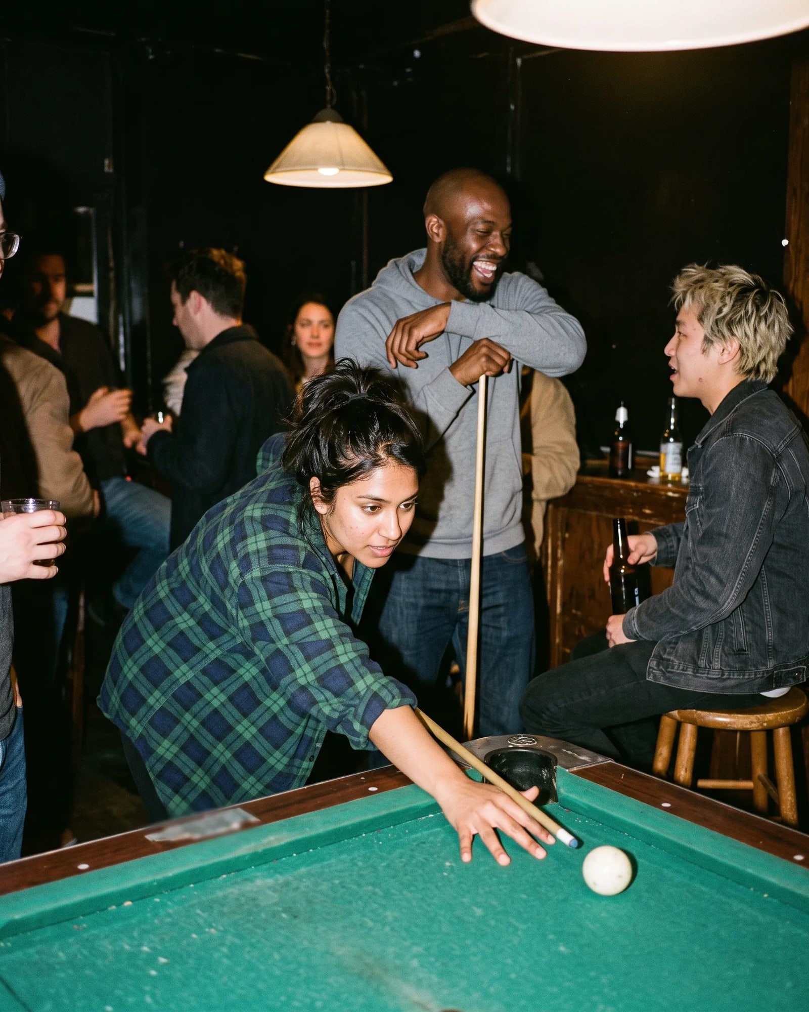 A woman lines up a pool shot while friends laugh behind her in a bar.