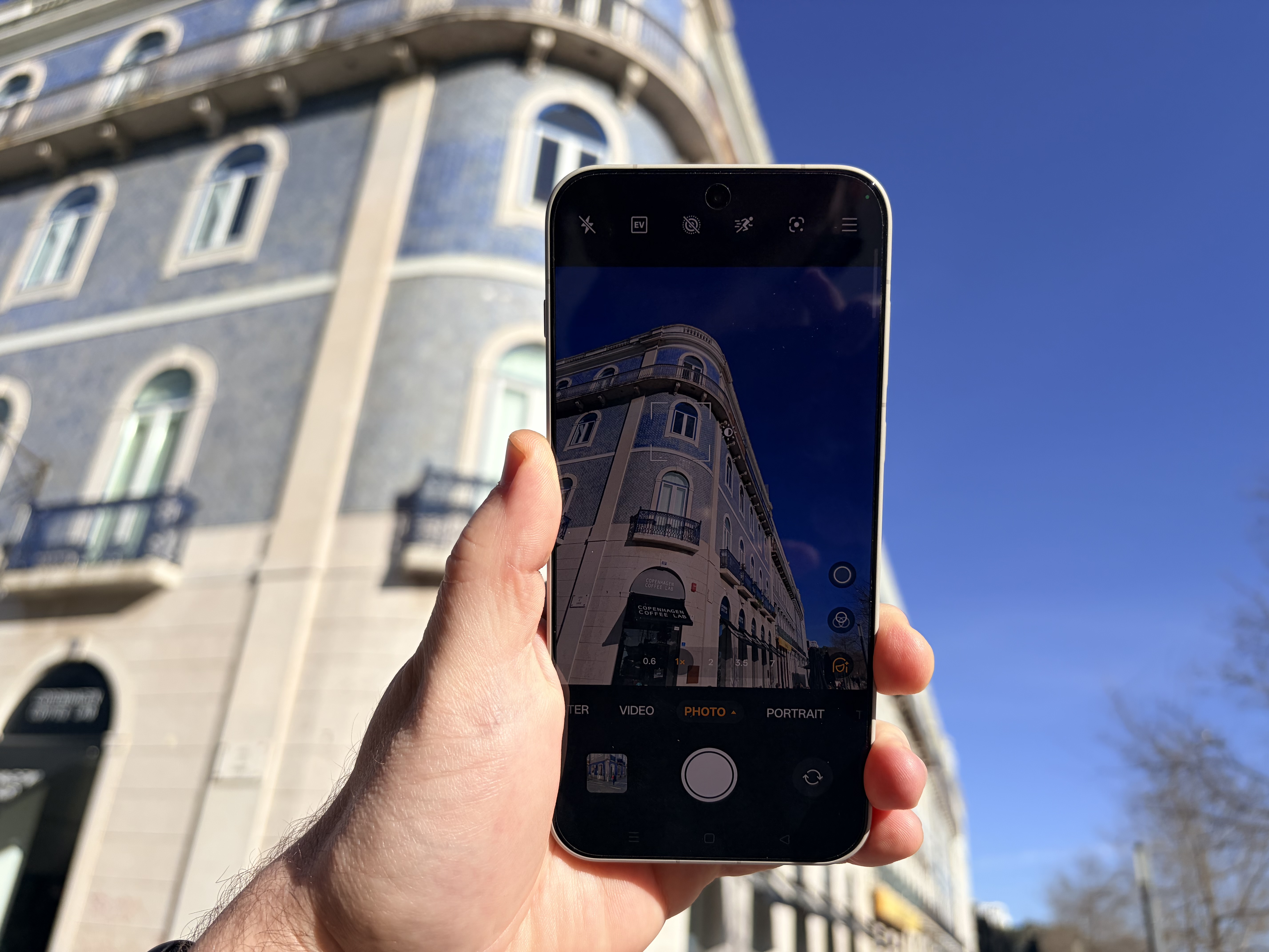 OnePlus 15 review, showing the screen brightness capability holding the phone outside against a blue sky in Lisbon. 