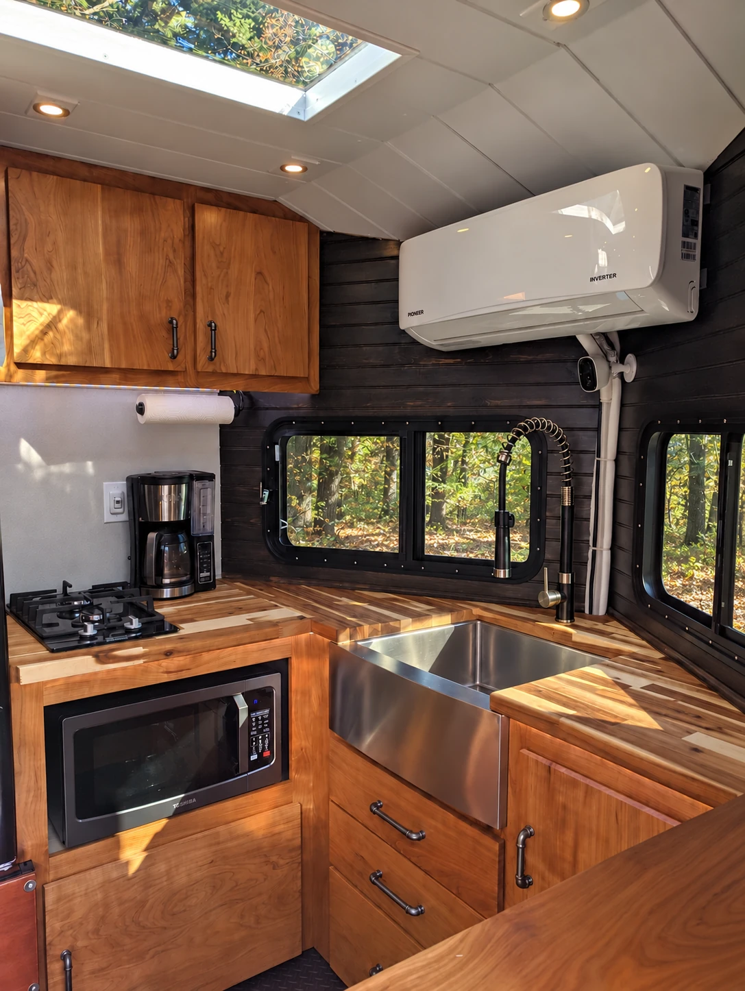 Cleaned photograph of the off-grid tiny home kitchenette, with farmhouse sink, cooktop, and wooded views through the windows