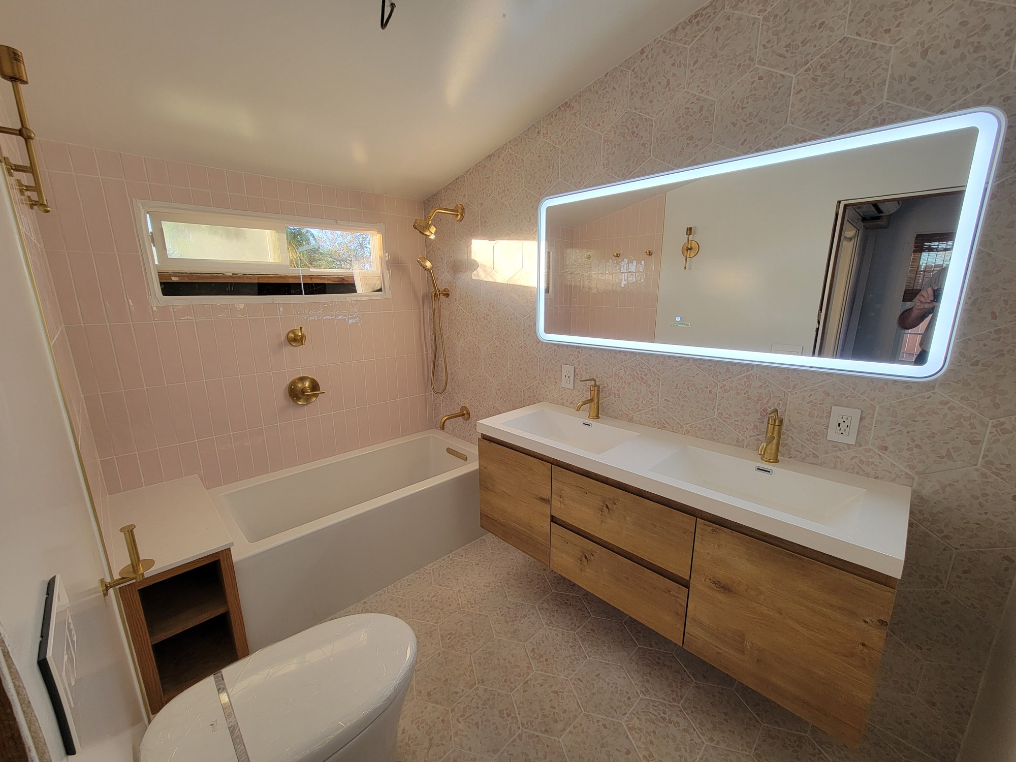 Completed Landers bathroom with pink tile, gold-tone fixtures, floating vanity and backlit mirror.