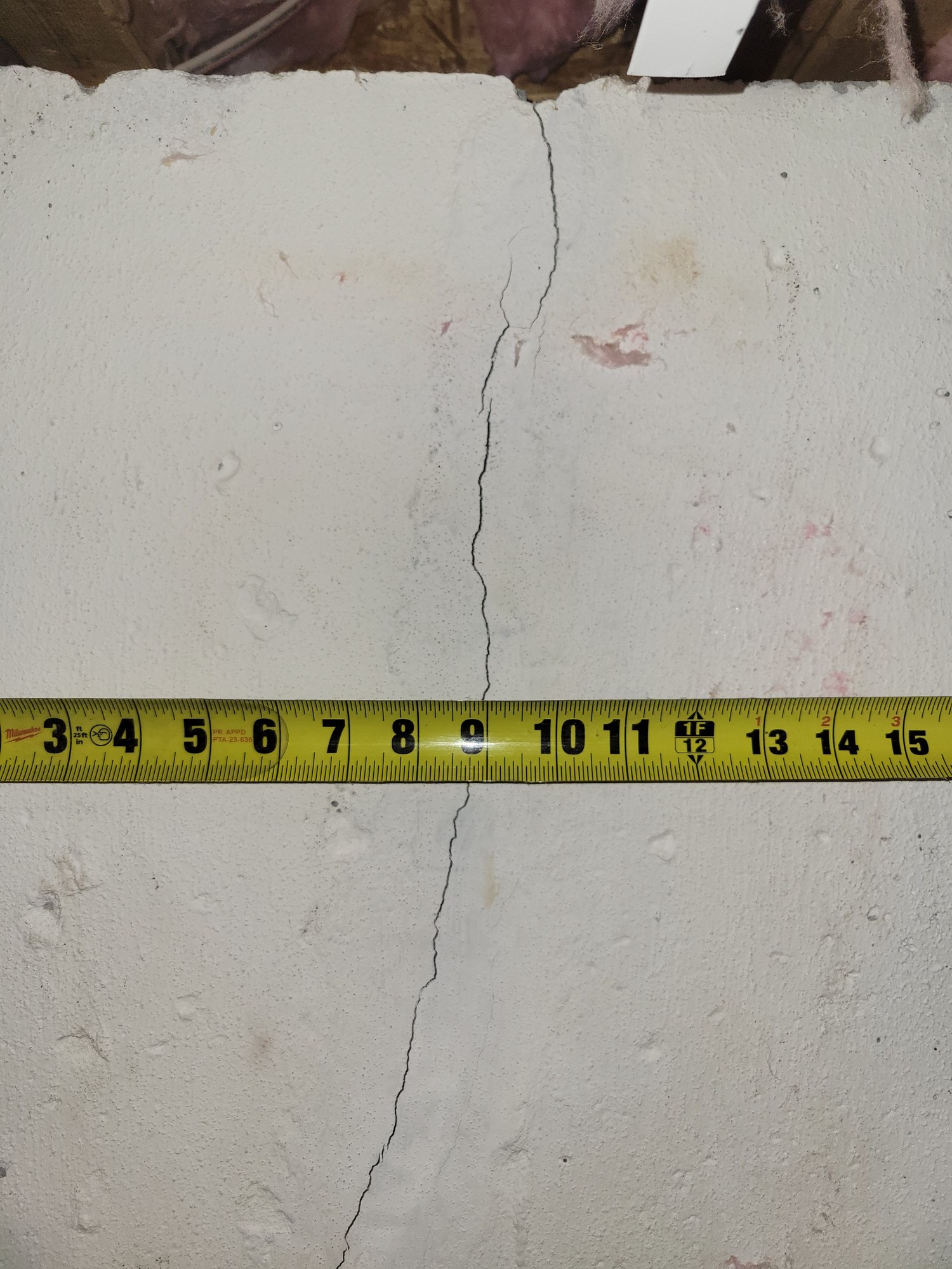 Close view of measured hairline crack in poured-concrete basement foundation wall.