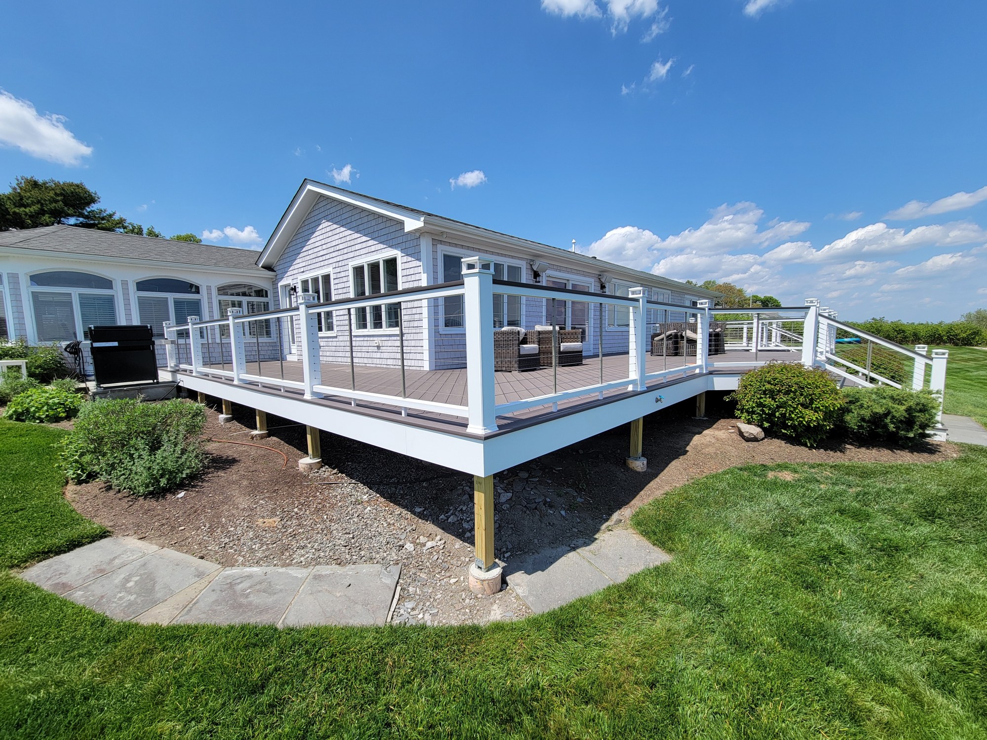 Three-quarter finished view of the Warwick Neck deck with cable railing and coastal surroundings.
