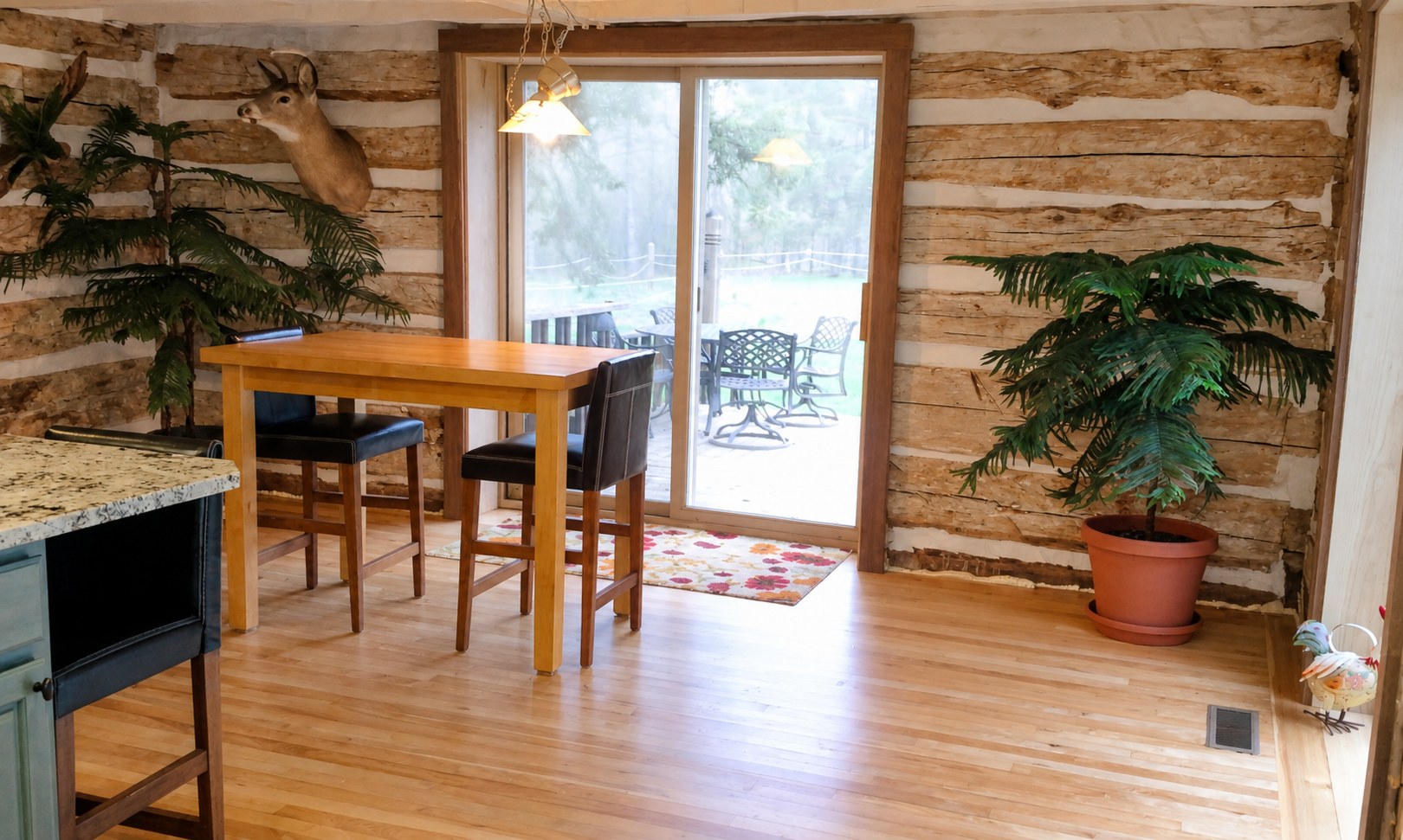 Finished historic farmhouse dining area with restored exposed log wall, table and patio doors; photograph enhanced for clarity.