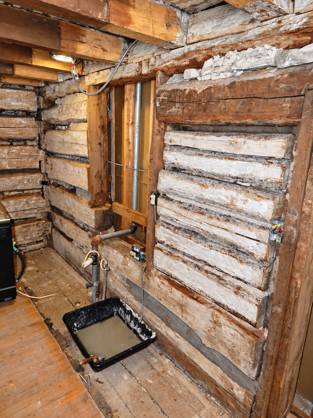 Historic log wall and chinking repair in progress around framing and services.