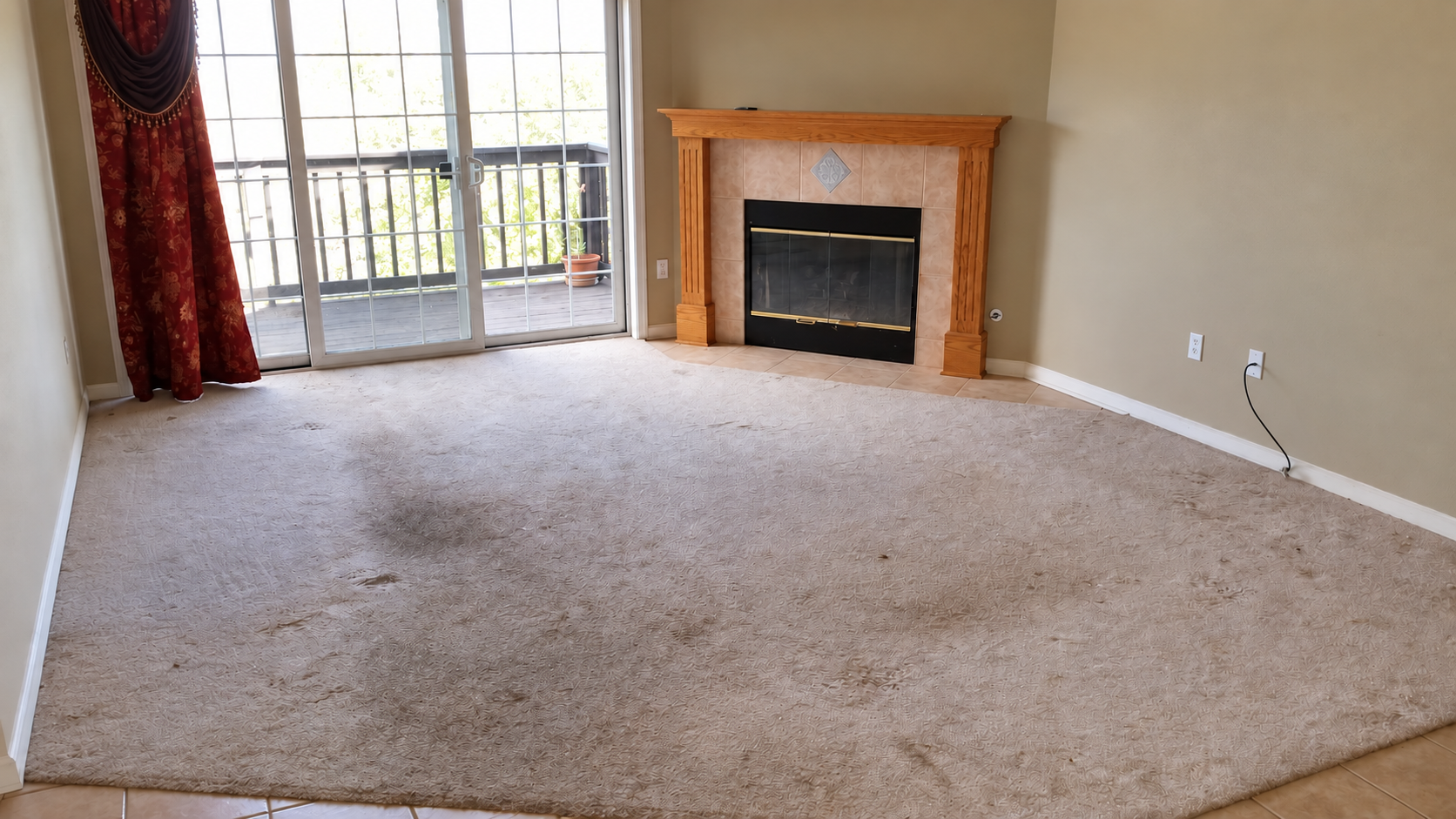 Pewaukee condo living room before renovation, with worn carpet, fireplace and patio door.