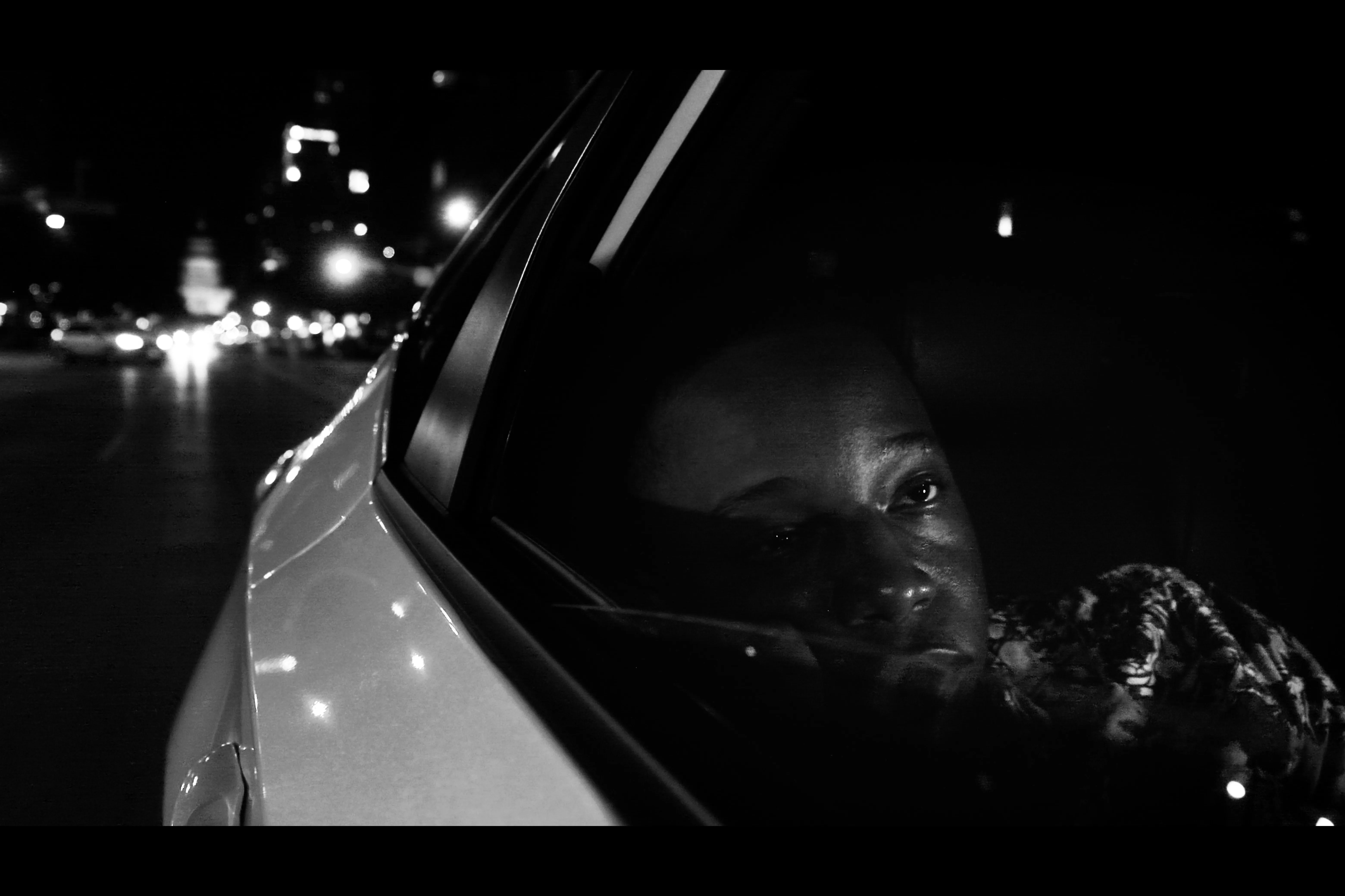 Otis looking out of a taxi window at night, city lights behind him